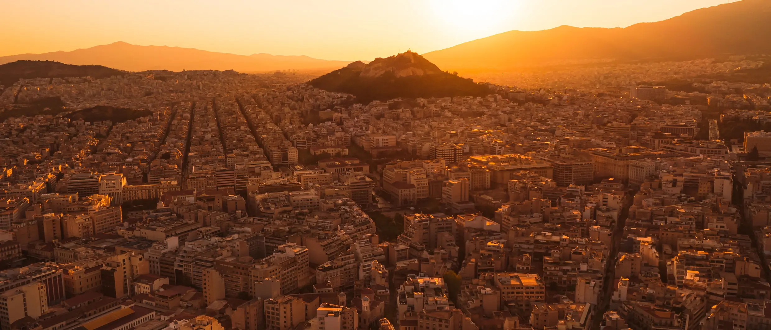 Athens at sunset, the city stretching to the mountains with Lycabettus hill in the middle distance