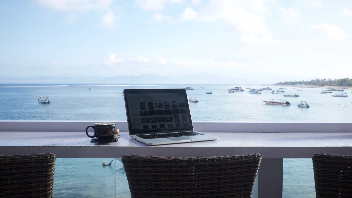 A laptop and a coffee cup on a table facing the sea and moored boats